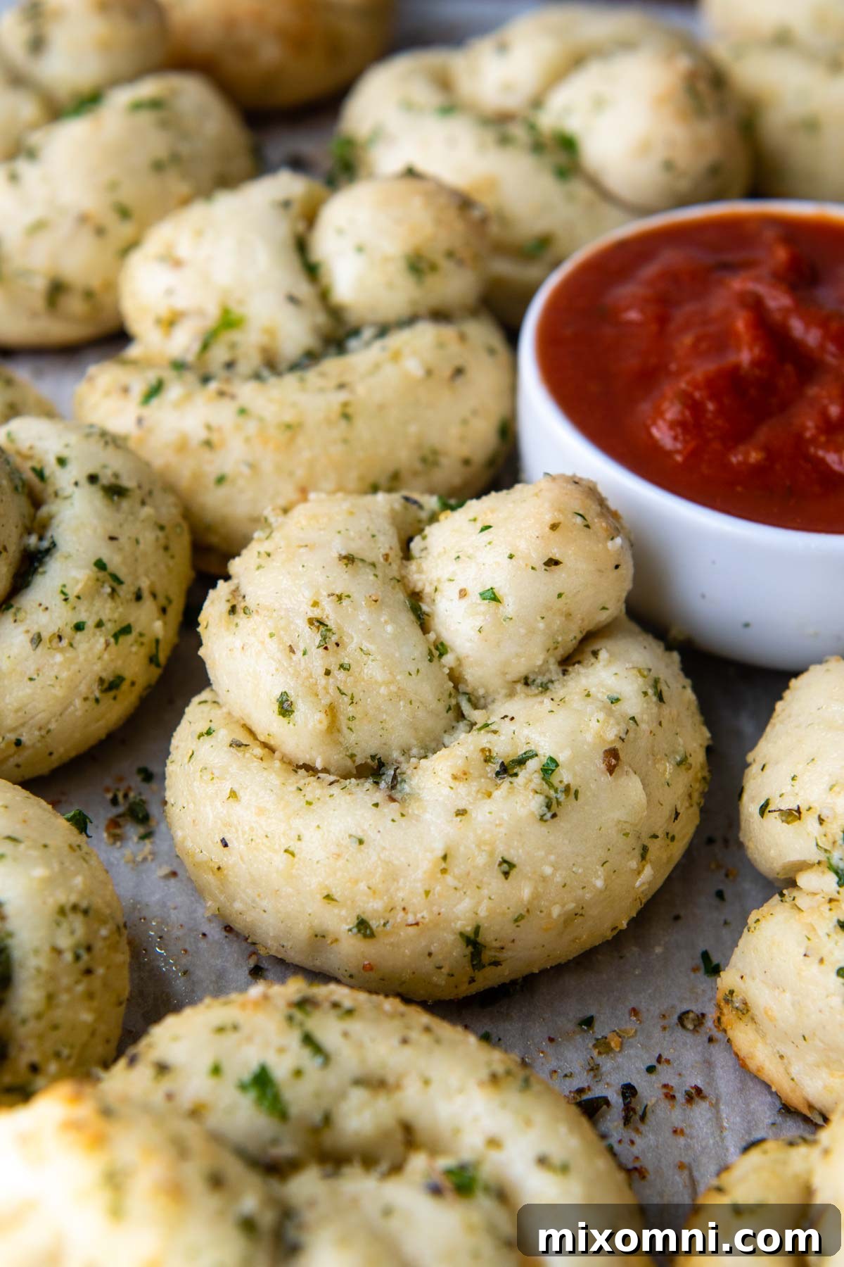 A cluster of freshly baked gluten-free garlic knots nestled together, with a small cup of vibrant marinara sauce placed beside them for dipping, highlighting a perfect serving suggestion.