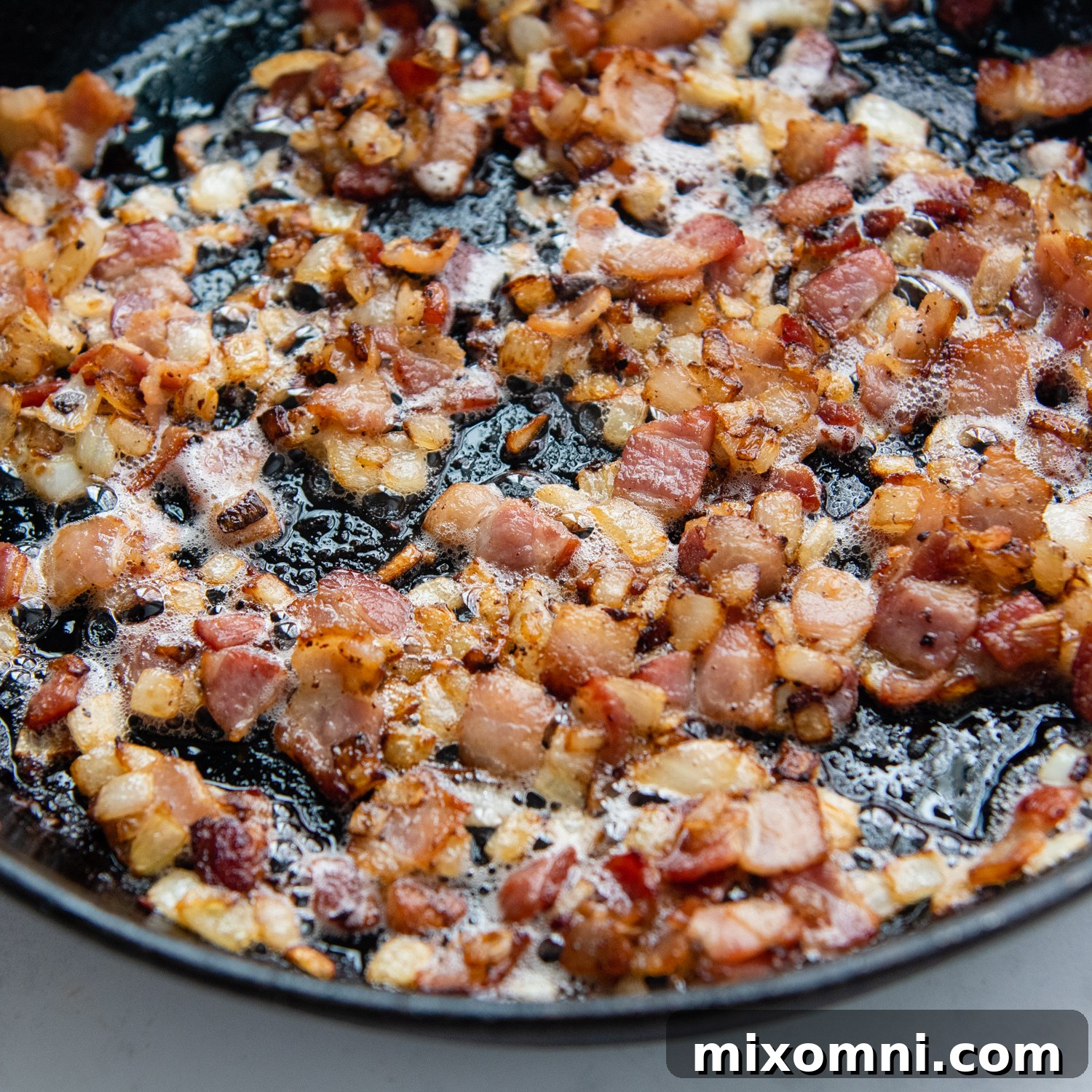 bacon and onions cooking in a cast iron skillet.