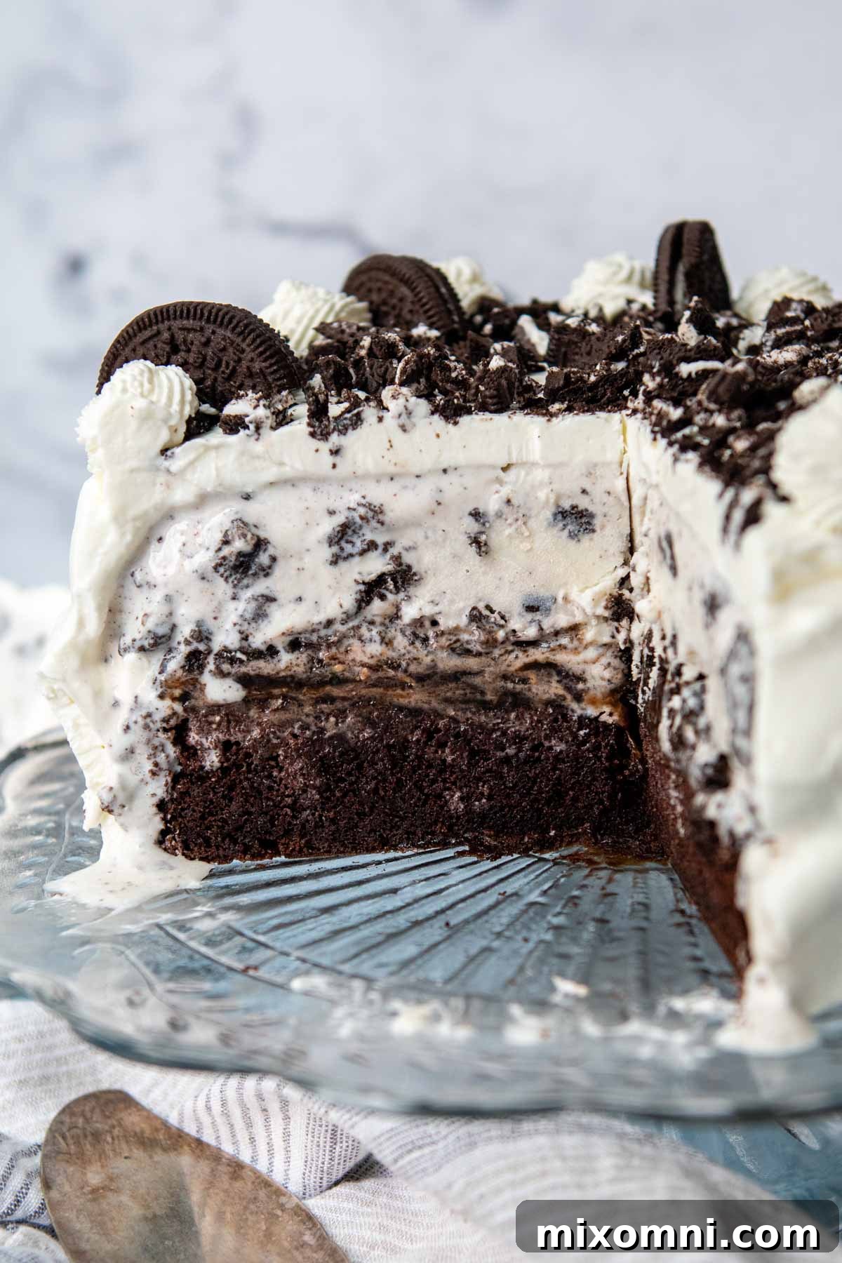 A decadent gluten-free Oreo ice cream cake on a cake stand with a slice removed, showcasing its delicious layers.