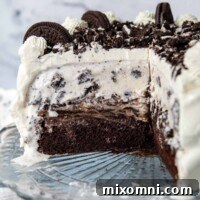 An Oreo ice cream cake on a cake stand with a slice out, showcasing its layers.