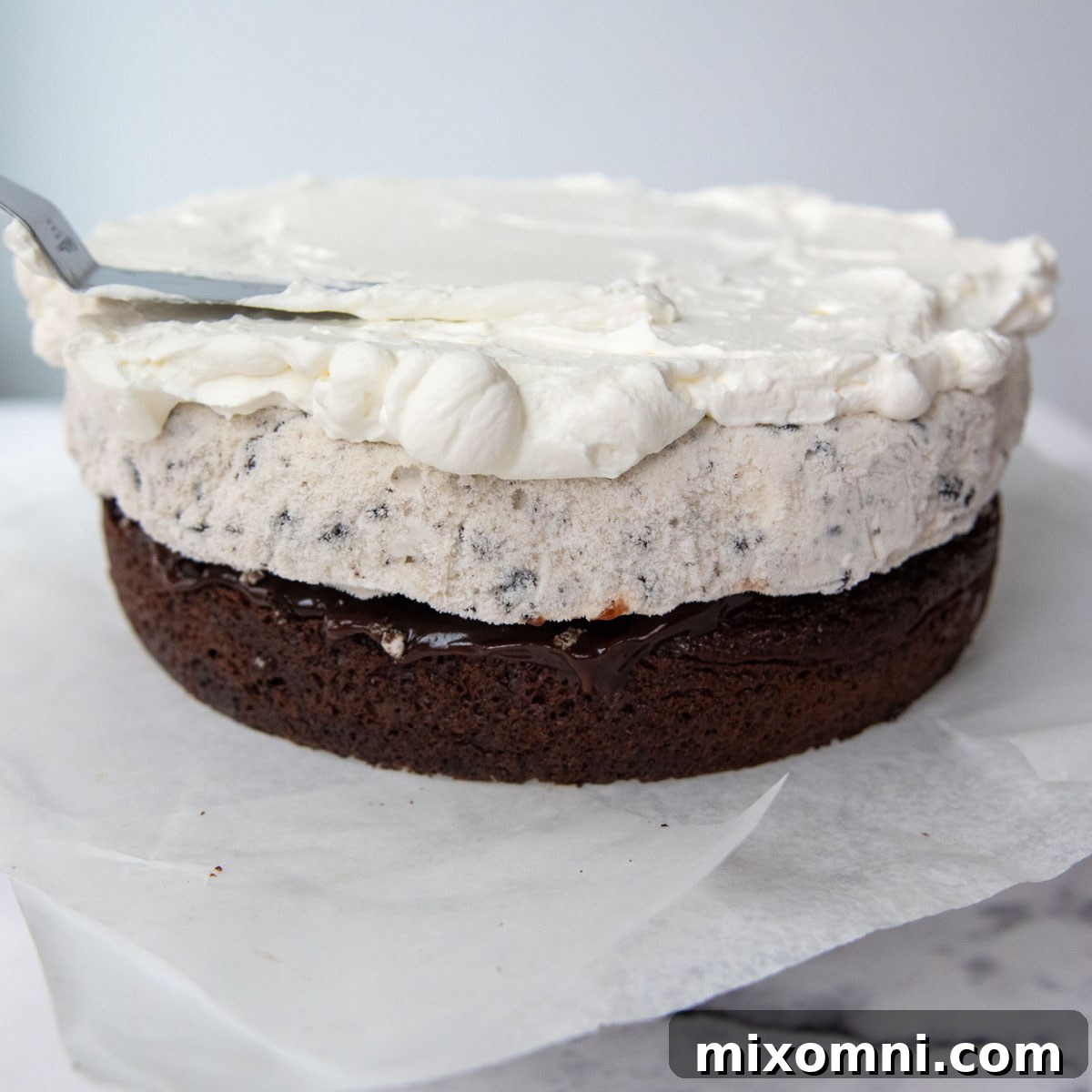 A layer of whipped cream frosting being spread smoothly over the ice cream layer.