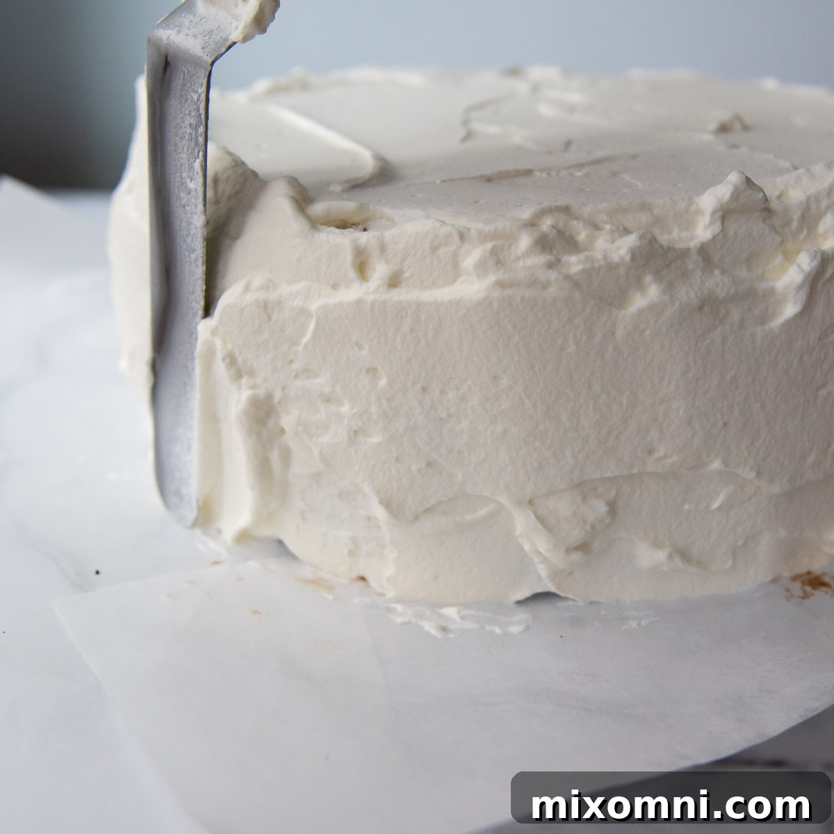 Whipped cream frosting being spread on the sides of the ice cream cake.
