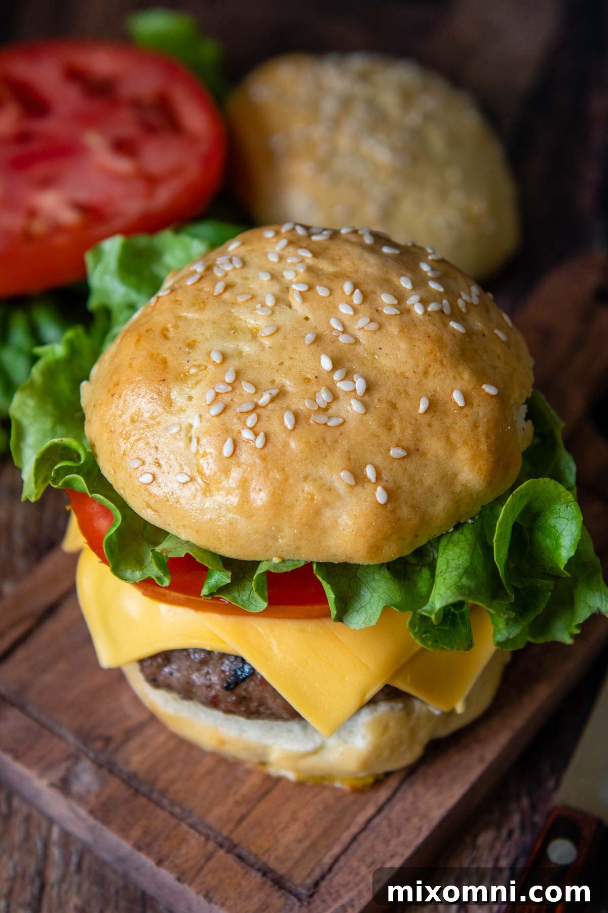 a burger with lettuce, tomato, and cheese on a wood cutting board.