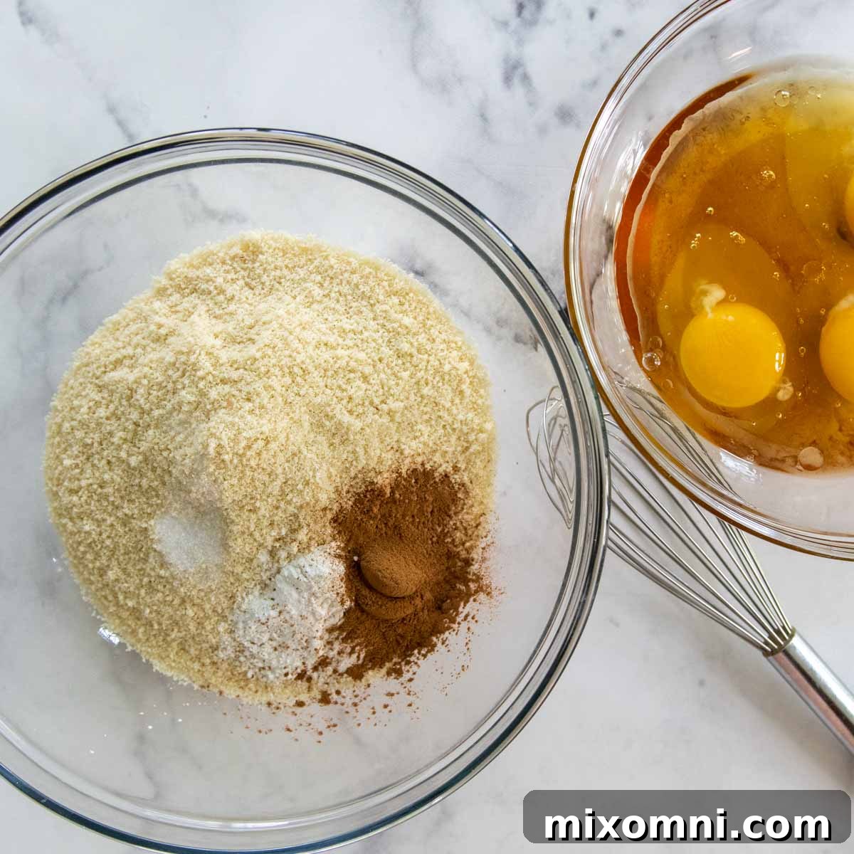Two separate bowls on a counter, one containing whisked dry muffin ingredients and the other whisked wet ingredients.