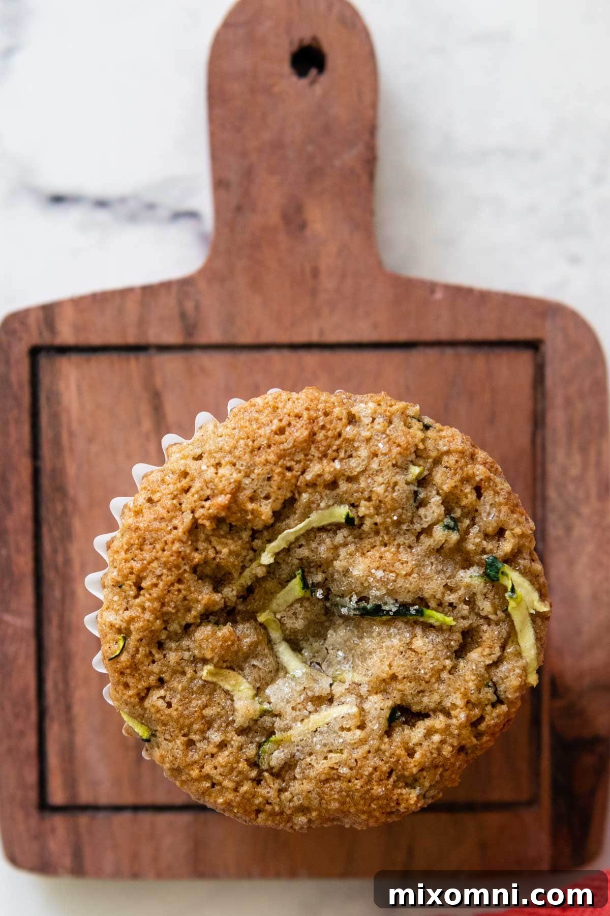 An overhead shot of a batch of golden-brown almond flour zucchini muffins cooling on a rustic wooden cutting board.