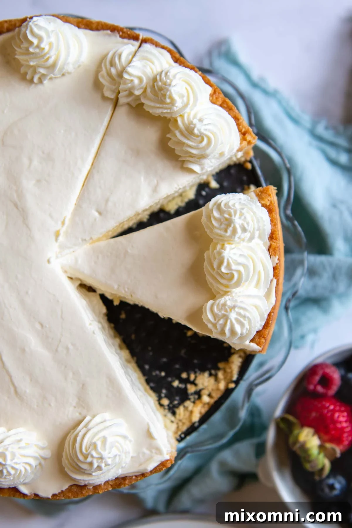 An overhead shot of a beautifully sliced gluten-free cheesecake, accompanied by a bowl of vibrant fresh berries, perfect for serving.