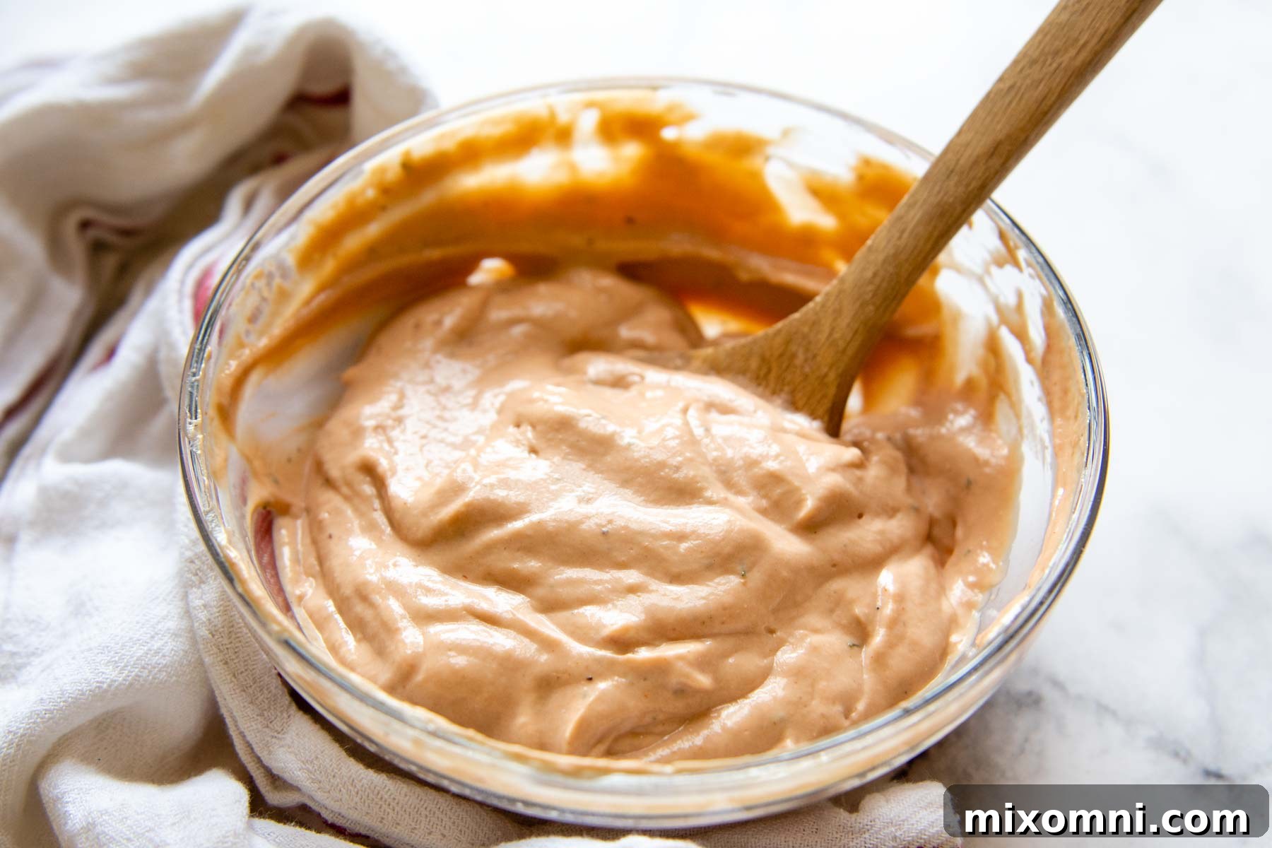 a glass bowl with bbq ranch sauce inside and towel laying next to it.