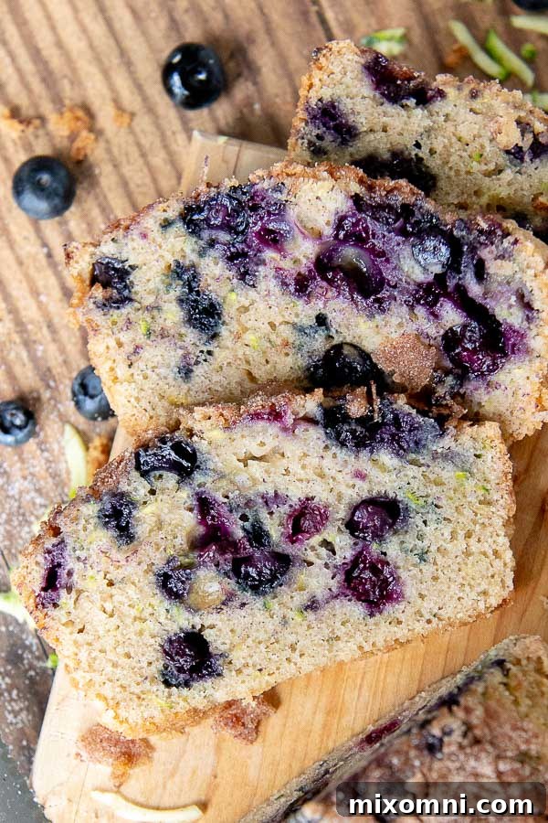 Overhead shot of perfectly baked slices of blueberry zucchini bread on a rustic cutting board, showcasing the moist interior, vibrant blueberries, and crunchy topping.