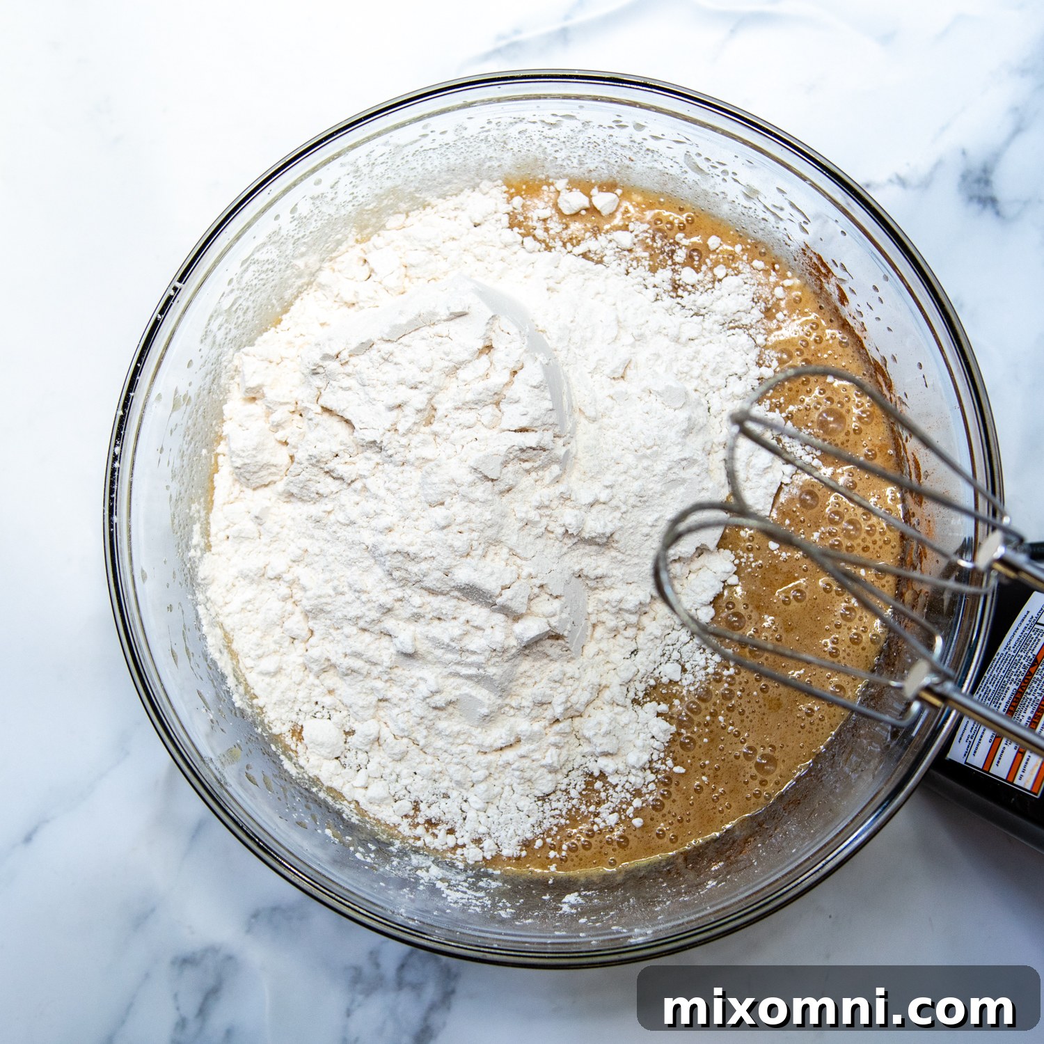 A large mixing bowl containing the wet ingredients with flour just mixed in, forming a smooth, thick batter.