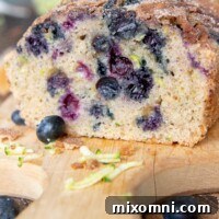 A loaf of blueberry zucchini bread on a cutting board with a slice taken out, showcasing the moist interior.