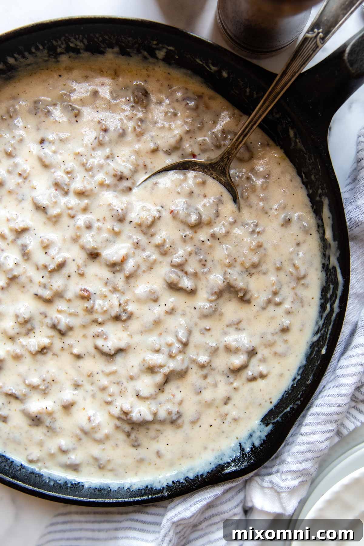 overhead shot of gluten-free sausage gravy in a rustic cast iron skillet, garnished with fresh parsley.