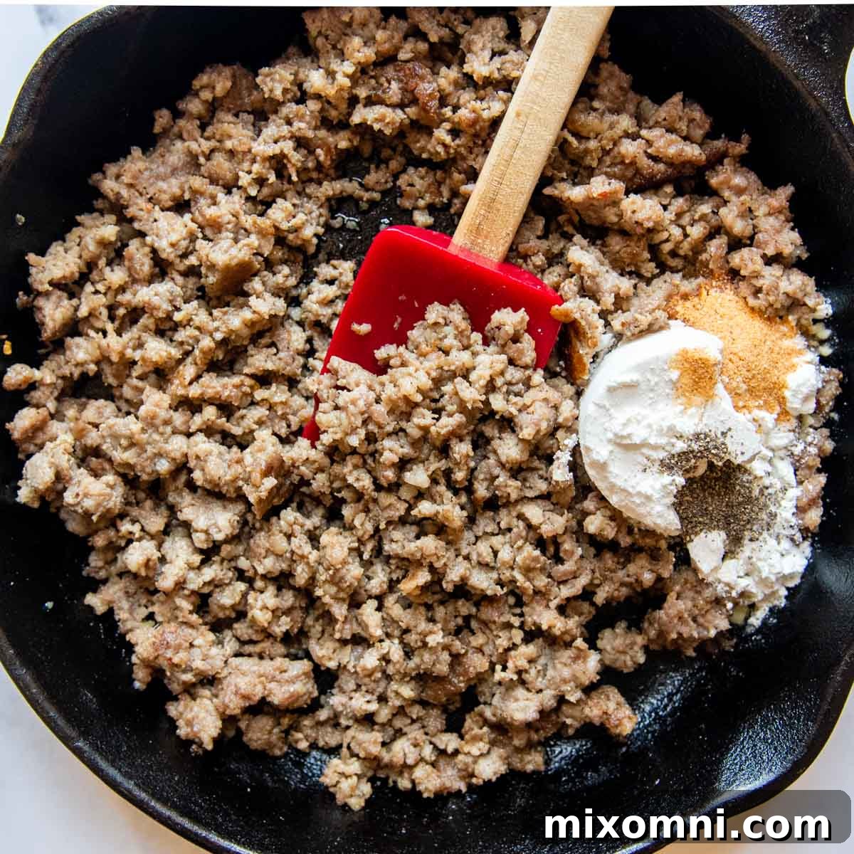 browned sausage in a skillet with flour and seasonings forming a roux.