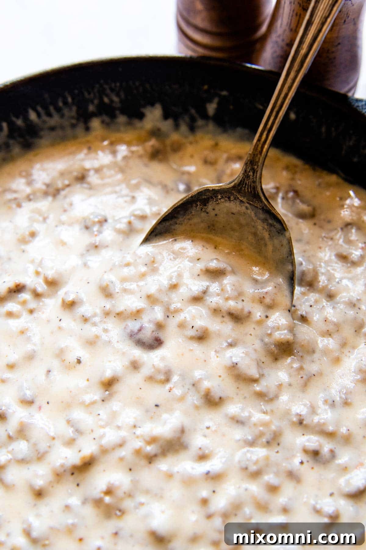 close up view of an antique spoon scooping into a cast iron skillet full of gluten-free sausage gravy.