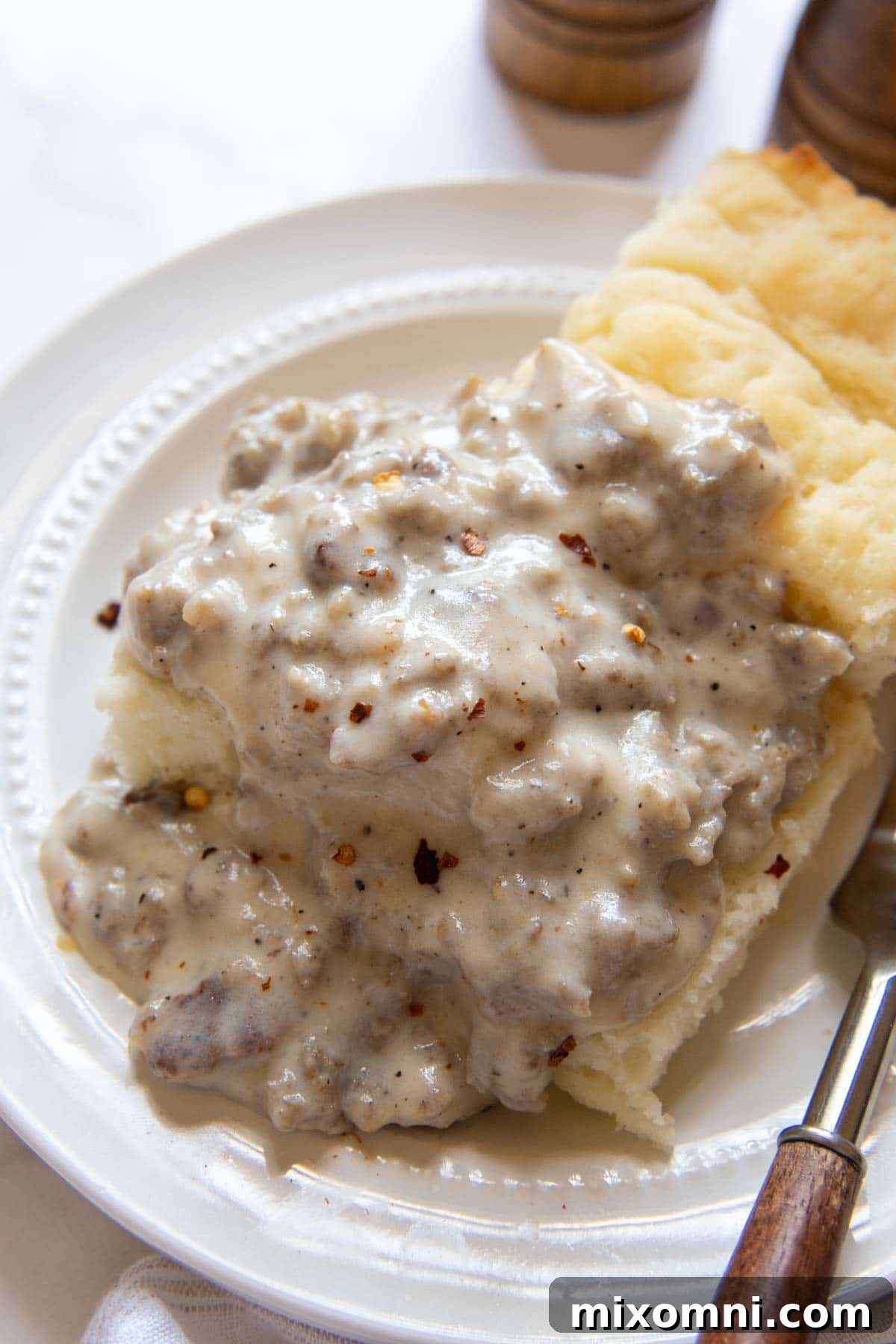 sausage gravy generously poured over two fluffy gluten-free biscuits on a white plate, ready to be served.