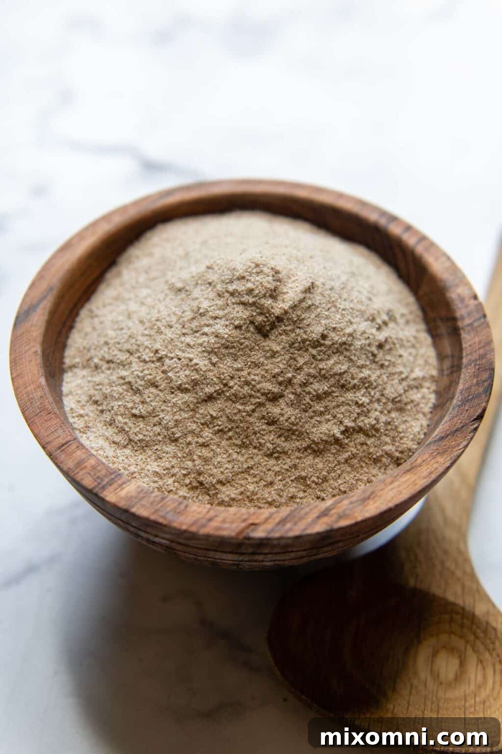 a wooden bowl of psyllium husk powder with spoon laying next to it