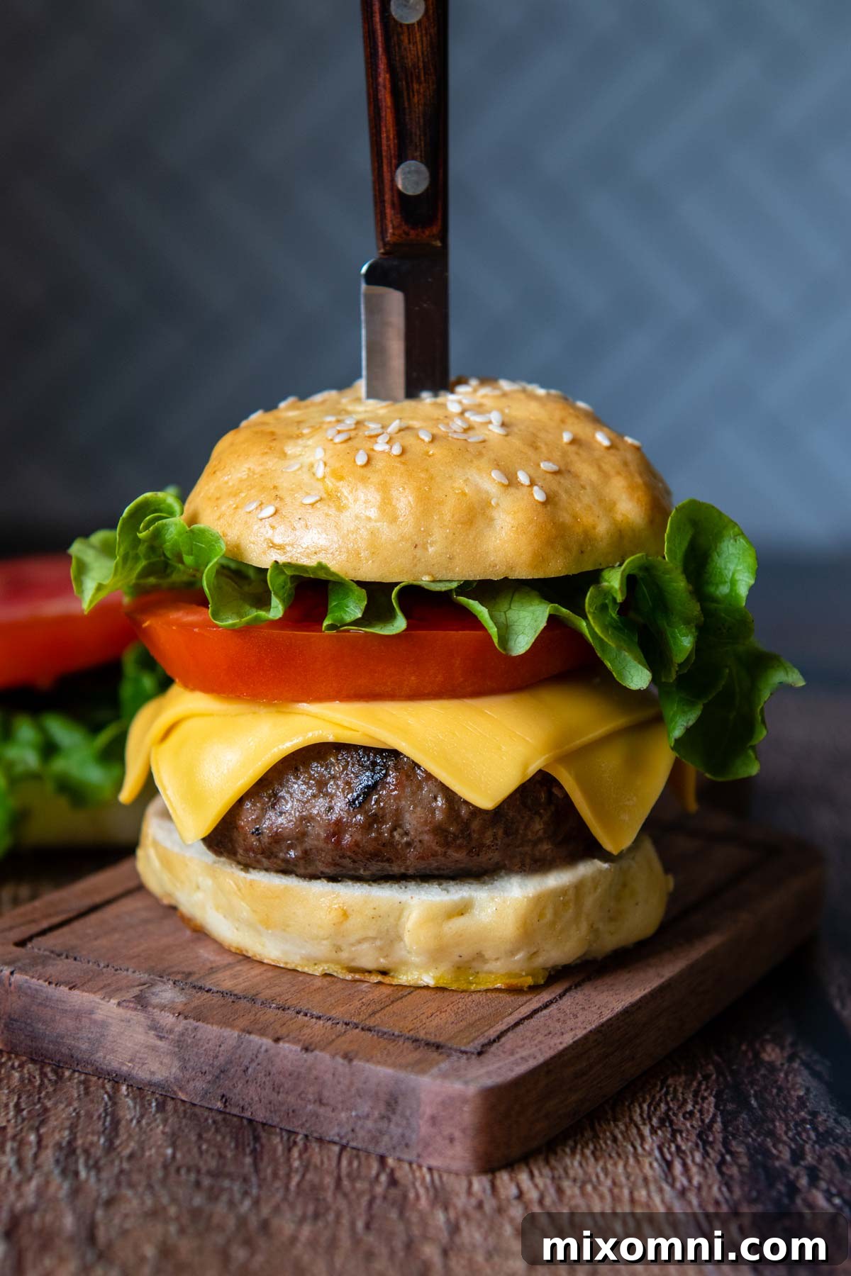 a straight on shot of an assembled burger with a knife stabbed into the top.
