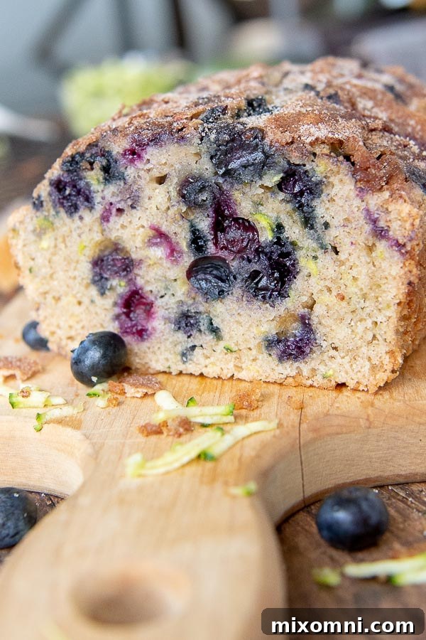 A loaf of blueberry zucchini bread on a cutting board with a slice already taken out.