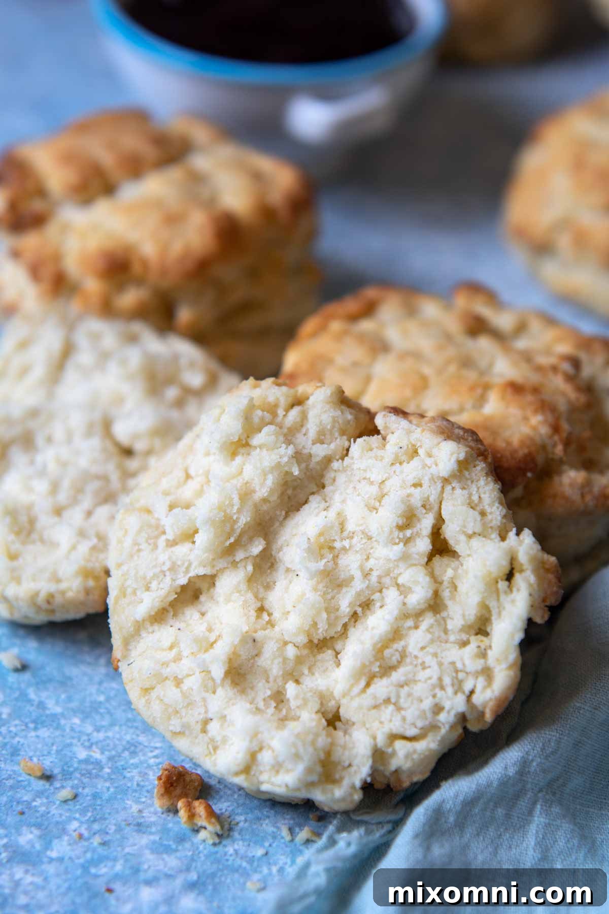 A perfectly split-open gluten-free biscuit, showing its light and fluffy interior, with a jar of jam gently blurred behind it.