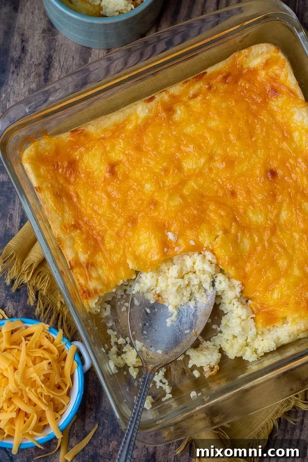 Overhead shot of a baked cheese grits casserole in a dish, with shredded cheese and a blue linen napkin placed beside it.