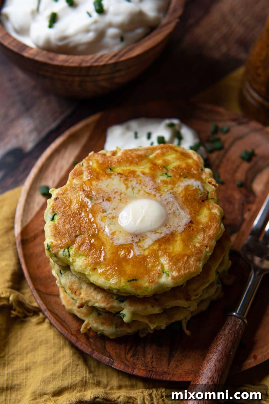 Side angle shot of freshly cooked gluten-free zucchini fritters piled on a plate, with butter melting on top, indicating they are hot and ready to eat.