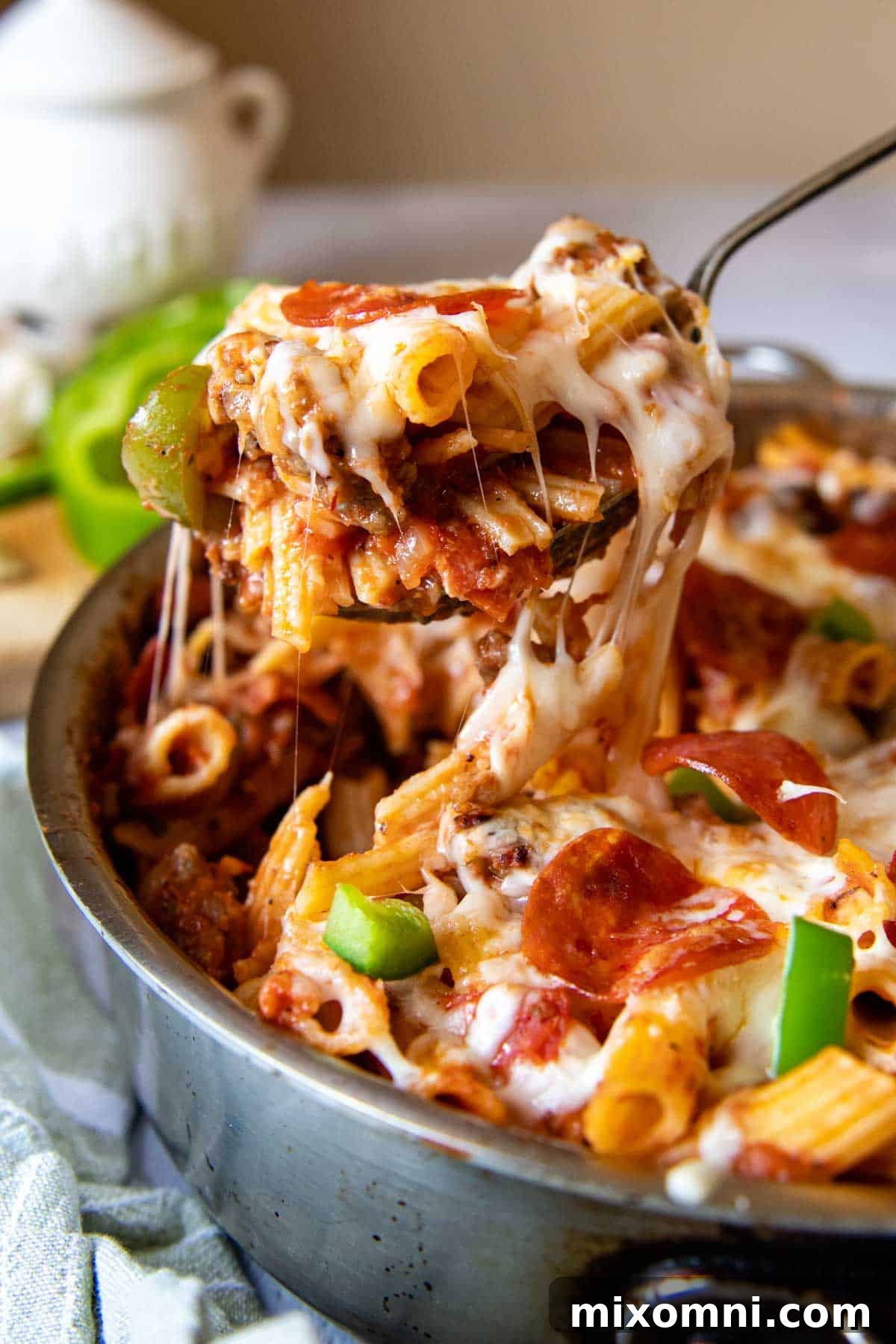 A serving spoon lifting out a generous portion of the cheesy, saucy Supreme Pizza Pasta Skillet from the pan.