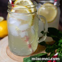 A Spiked Lemon Shake-Up Cocktail in a jar glass on a wooden coaster with red and white striped straws.