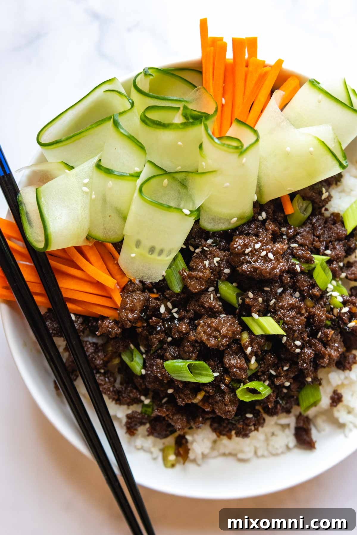 Overhead shot of a vibrant ground beef bulgogi bowl, garnished with crisp carrots, fresh green onions, and refreshing cucumber slices, ready to be enjoyed.