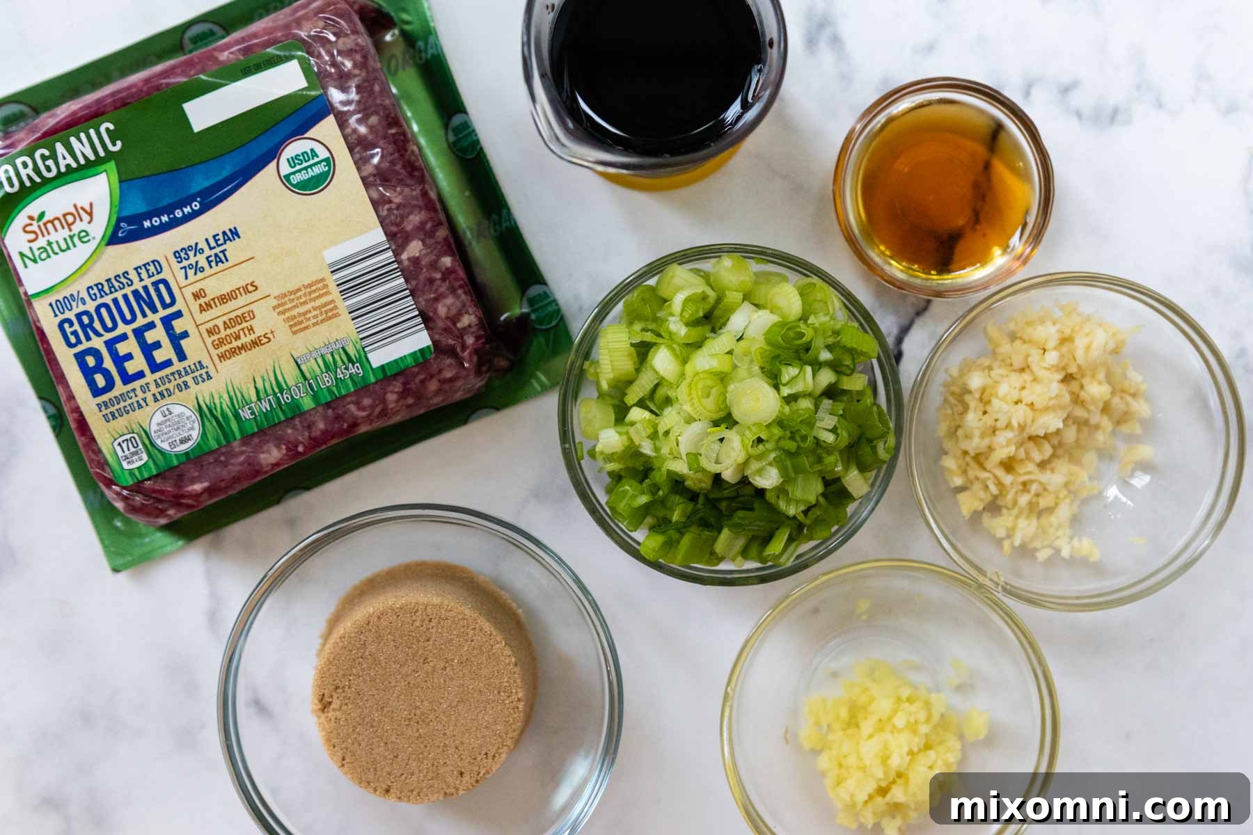 A collection of fresh ingredients laid out on a cutting board, including ground beef, garlic, ginger, soy sauce, brown sugar, and green onions, poised for making Korean ground beef bulgogi.