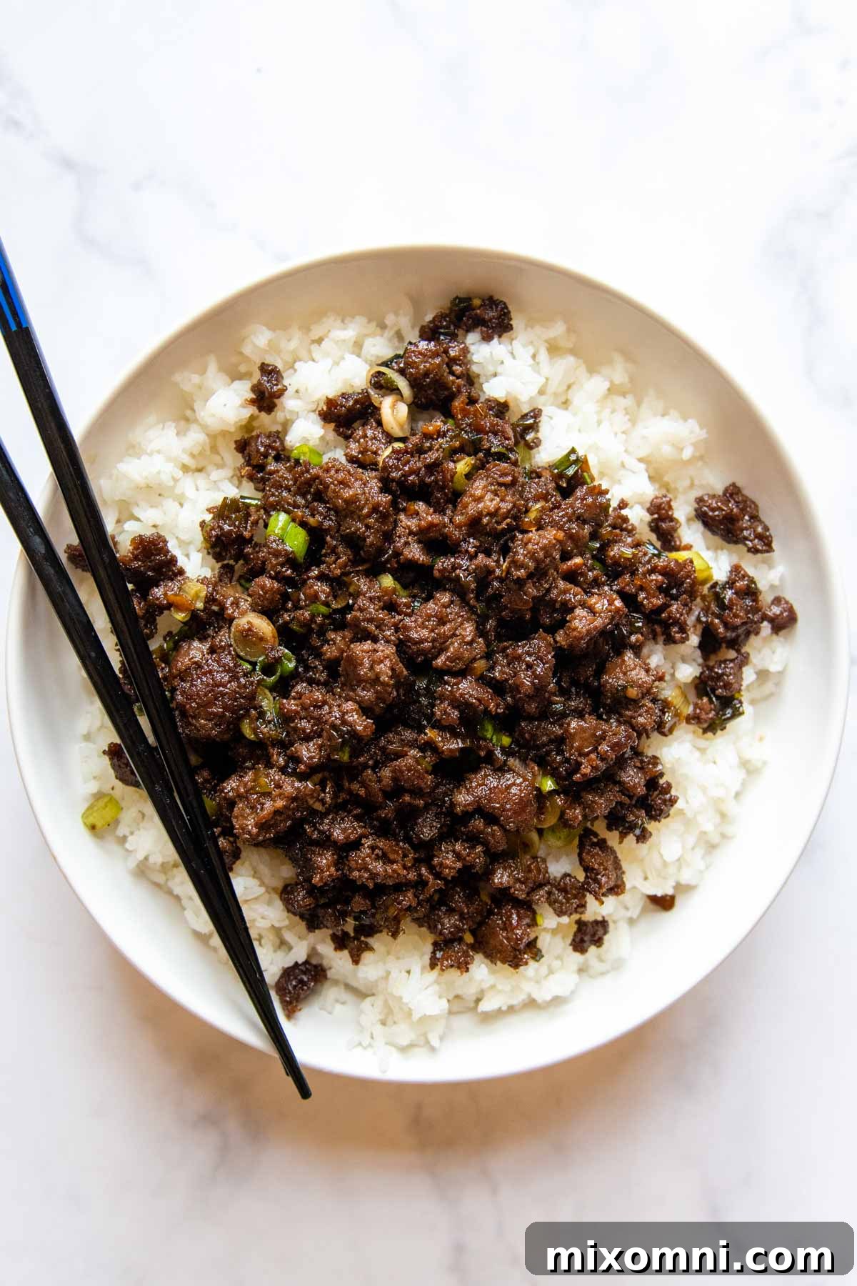 An inviting overhead view of a bulgogi bowl, elegantly served over white rice and accompanied by chopsticks on a pristine white background, showcasing its delicious appeal.