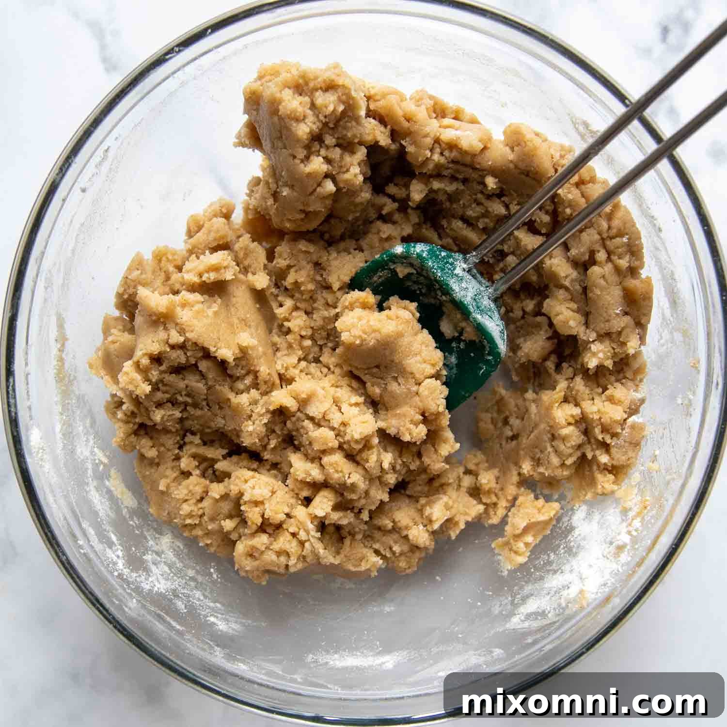 Thick, crumbly gluten-free streusel topping mixture in a glass bowl, being mixed together with a spoon.