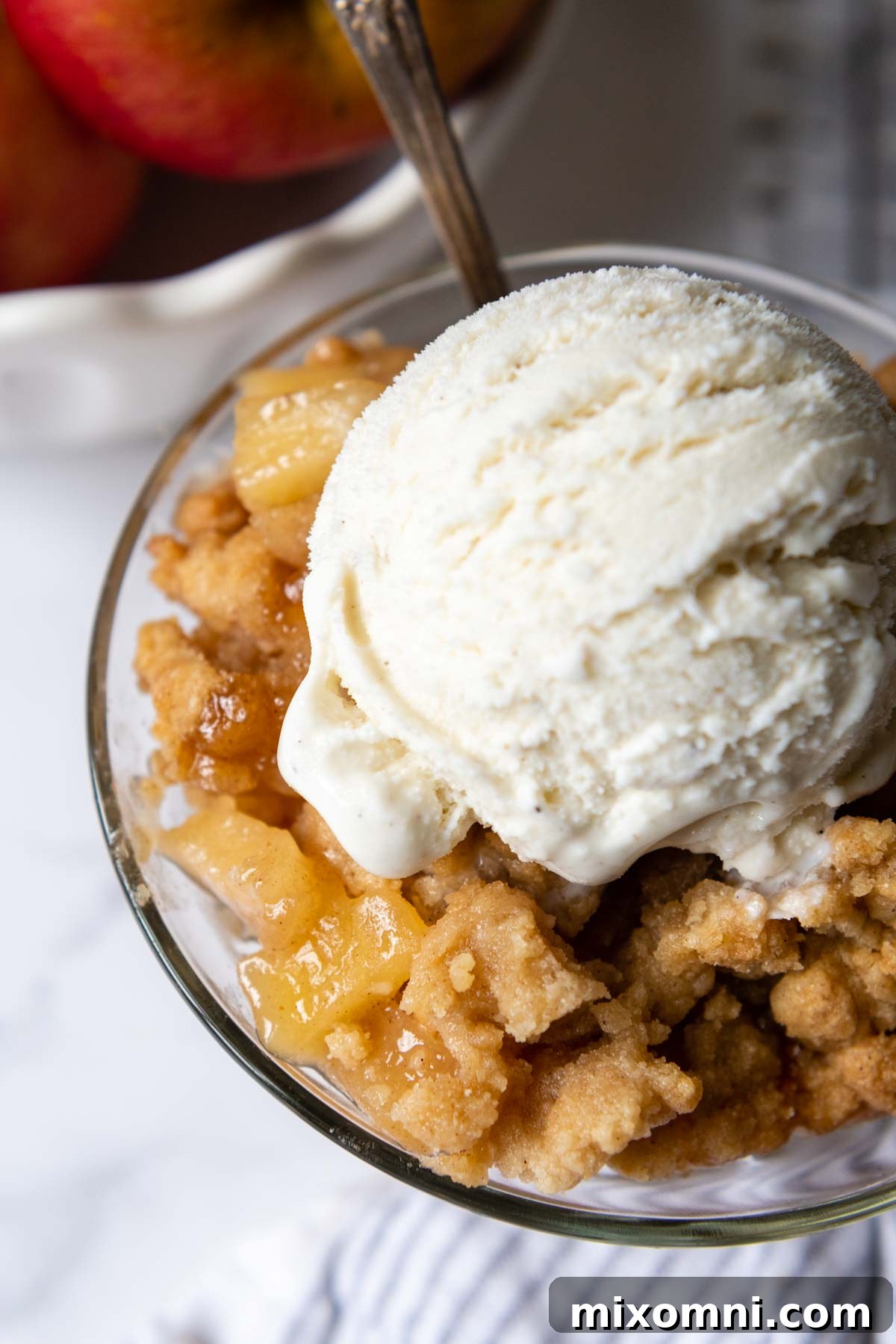 Overhead shot of a rustic gluten-free apple crisp in a glass baking dish, served with a generous scoop of vanilla ice cream on top.