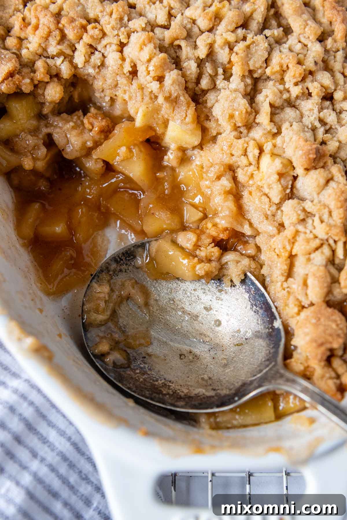 A spoon gently scooping into a close-up of warm gluten-free apple crisp, showing the tender apple filling and crunchy topping.