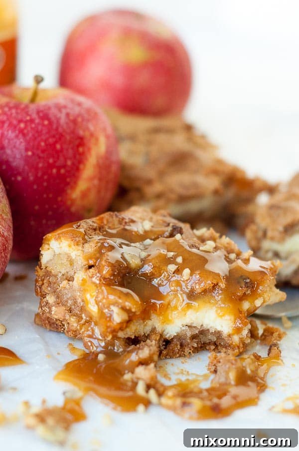 a bite taken out of an apple bar with cheesecake filling and caramel dripping over
