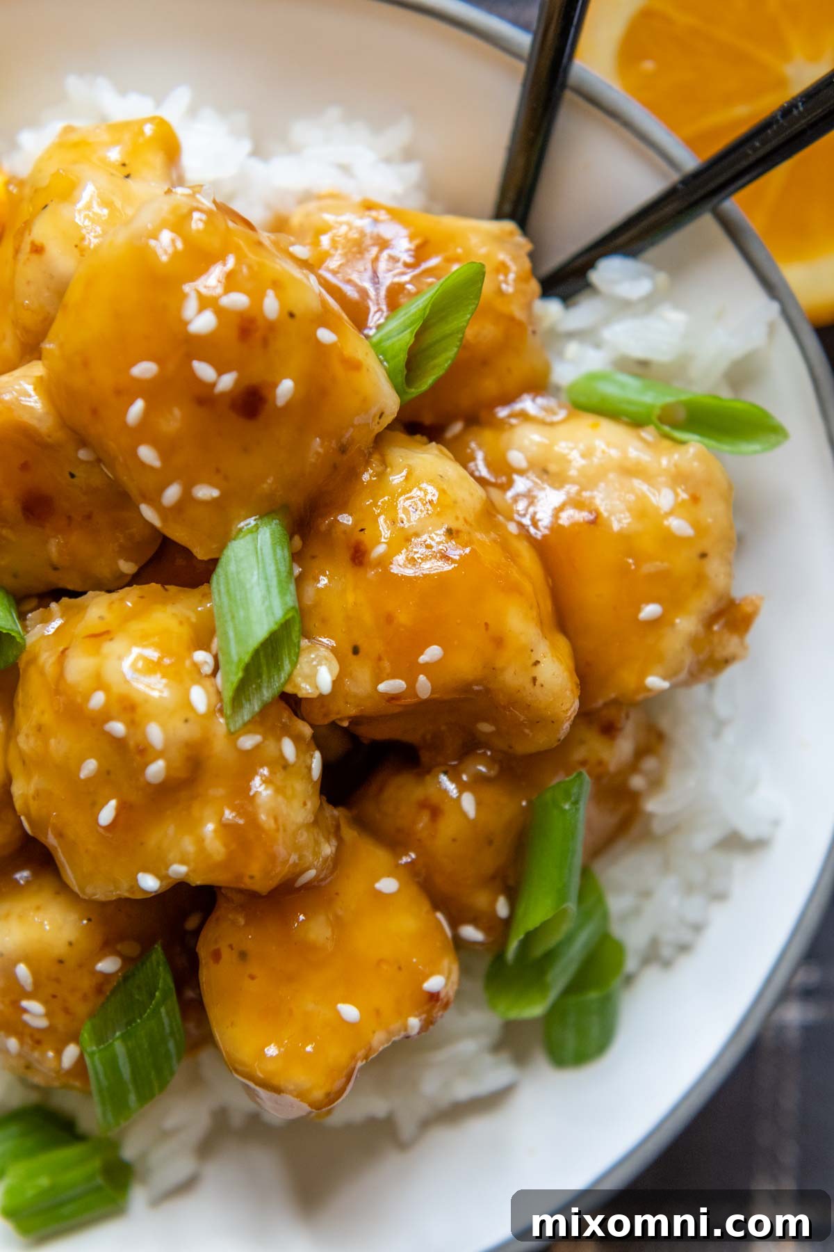 Close-up shot of crispy chicken pieces coated in vibrant orange sauce, ready to be served.