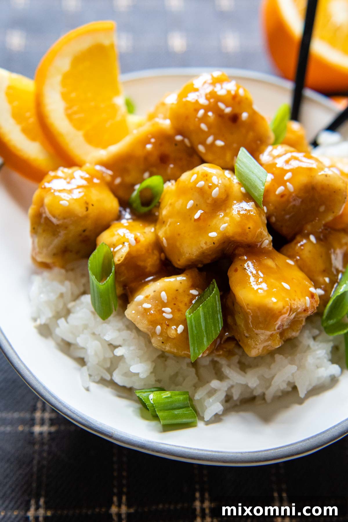 Gluten-free orange chicken served in a white bowl, garnished with fresh orange slices and chopped green onions.