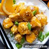 Overhead shot of a serving of gluten free orange chicken in a white bowl with chopsticks.
