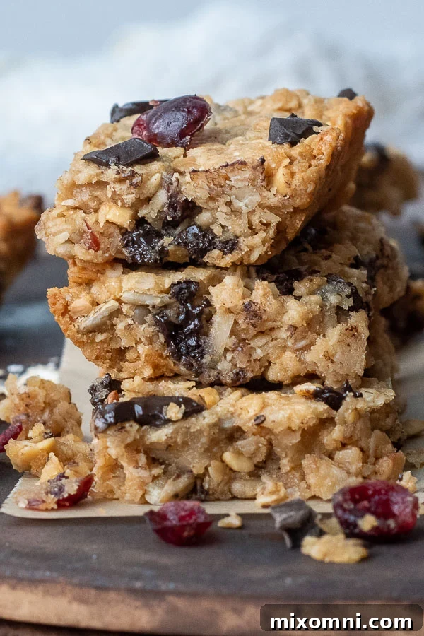 Stack of three homemade gluten-free chocolate chip granola bars with bits crumbling off, showcasing their chewy texture and delicious ingredients.