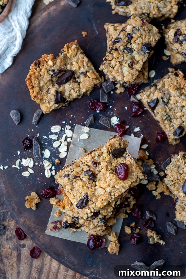 Overhead shot of perfectly cut homemade gluten-free chocolate chip granola bars, surrounded by scattered ingredients like oats, chocolate chips, and dried cranberries, highlighting their customizable nature.