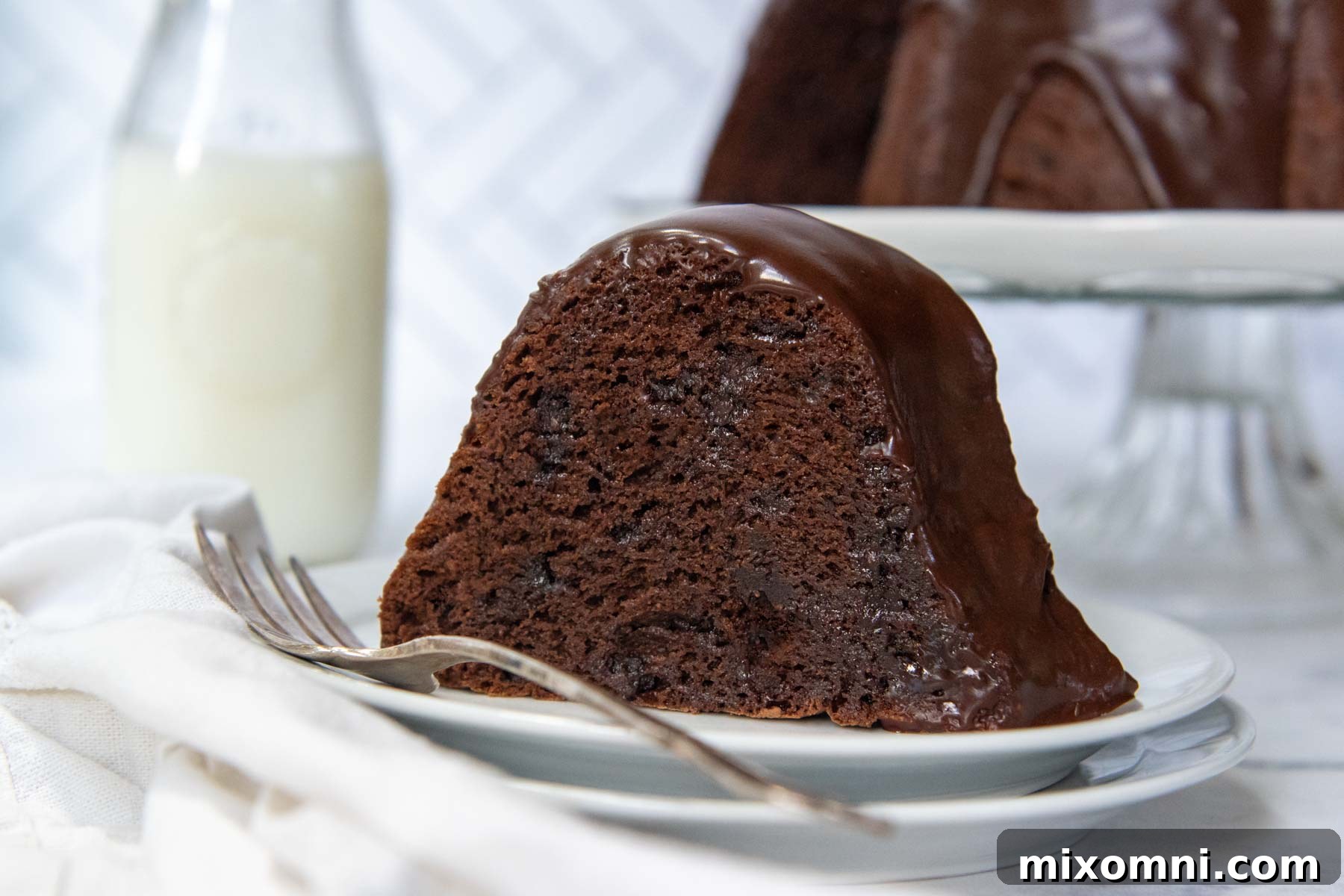 A slice of gluten-free chocolate bundt cake served on a white plate with a glass of milk in the background.