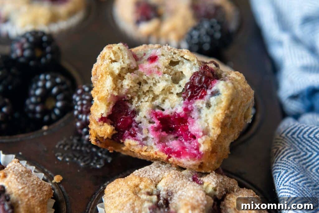 A perfectly baked gluten-free blackberry muffin with a bite taken out, showcasing its moist interior and juicy berries, resting invitingly on a muffin tin.