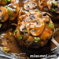 A spoon lifting a Salisbury steak with mushrooms from a skillet.