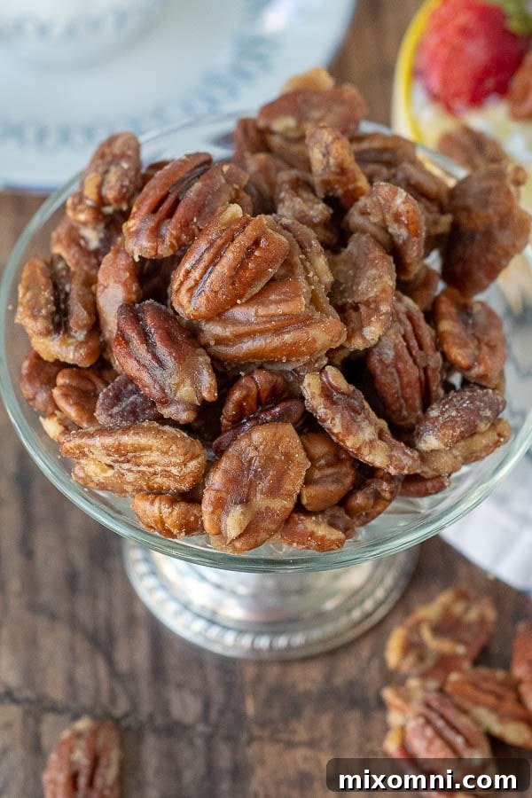 An overhead view of golden-brown candied pecans artfully arranged in an antique silver bowl, showcasing their glistening, caramelized coating.