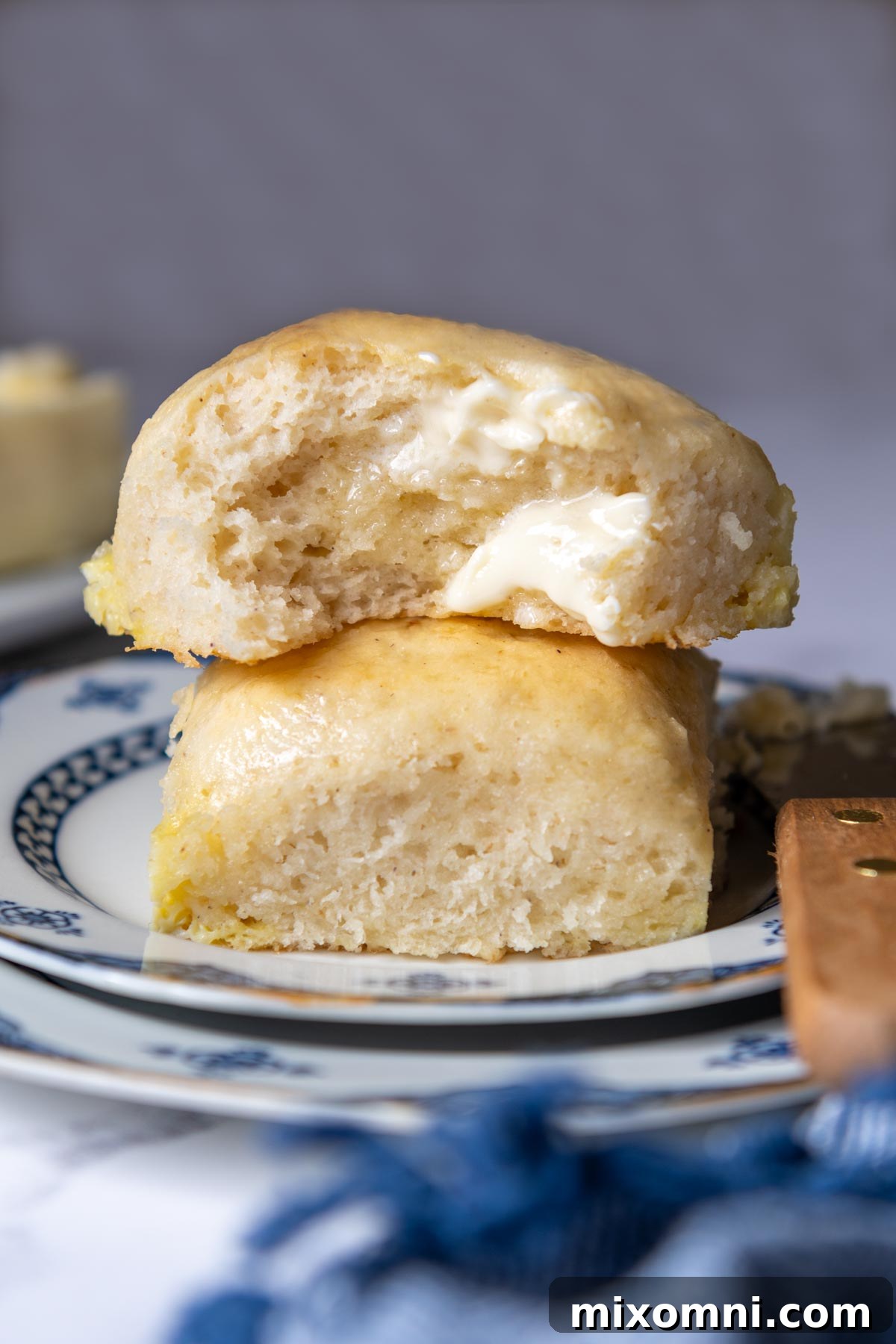 A perfectly golden gluten-free roll, torn open with melted butter, showcasing its soft, airy interior.