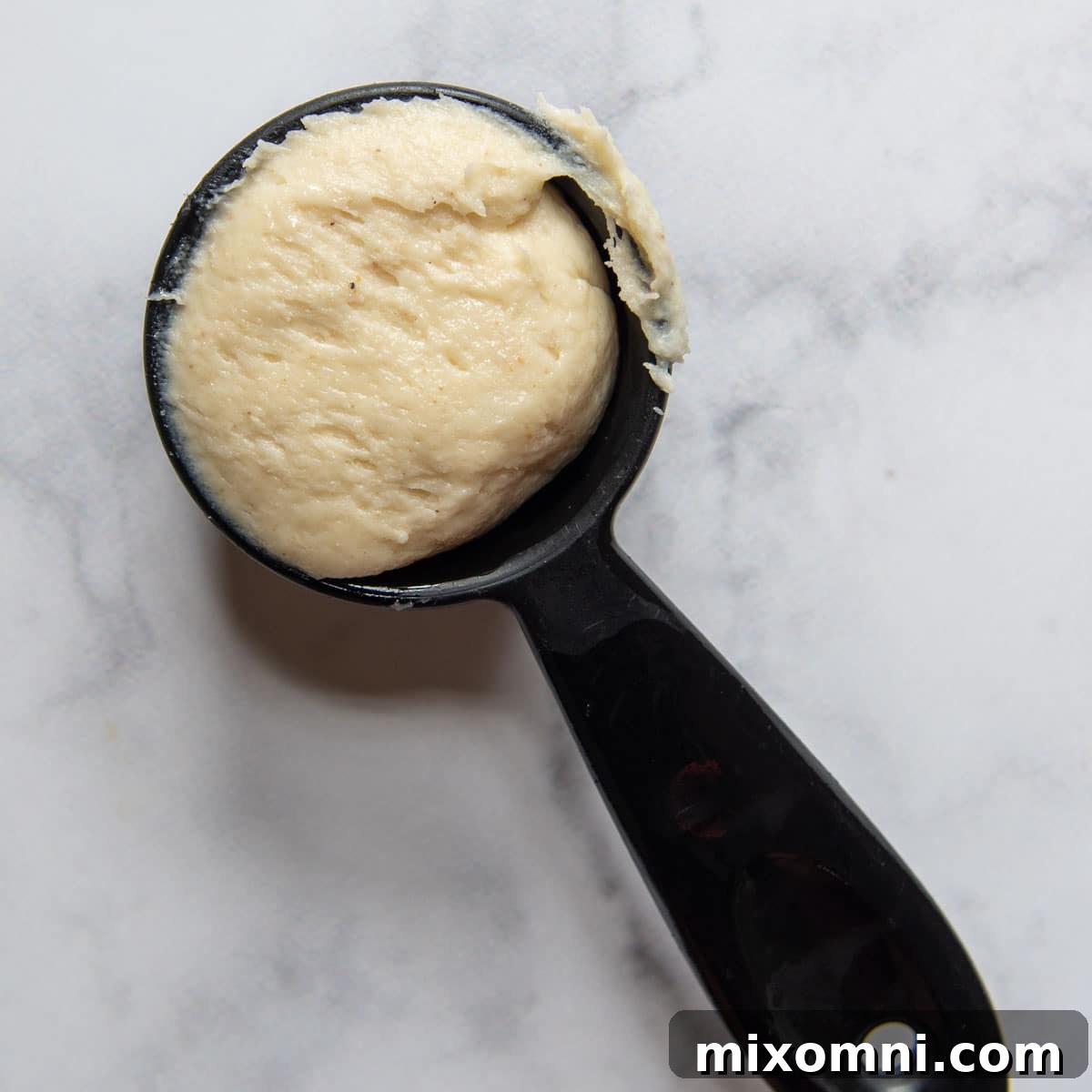 A measuring cup filled with gluten-free roll dough, demonstrating the easy shaping method.