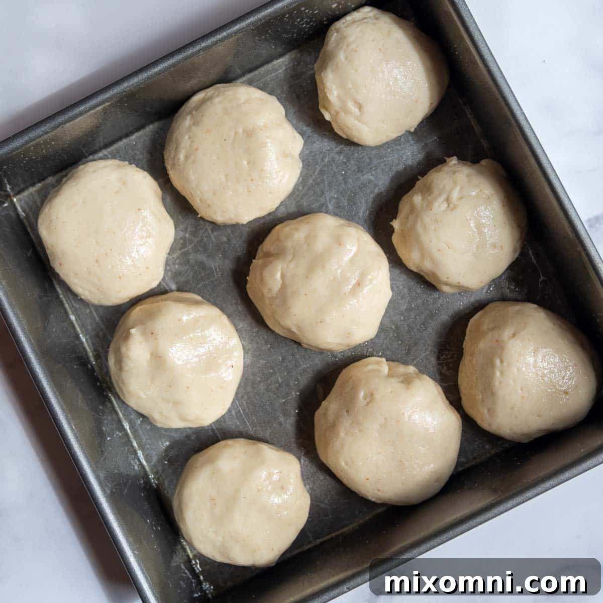 Unbaked gluten-free dinner rolls arranged in a baking pan, prior to their rise.