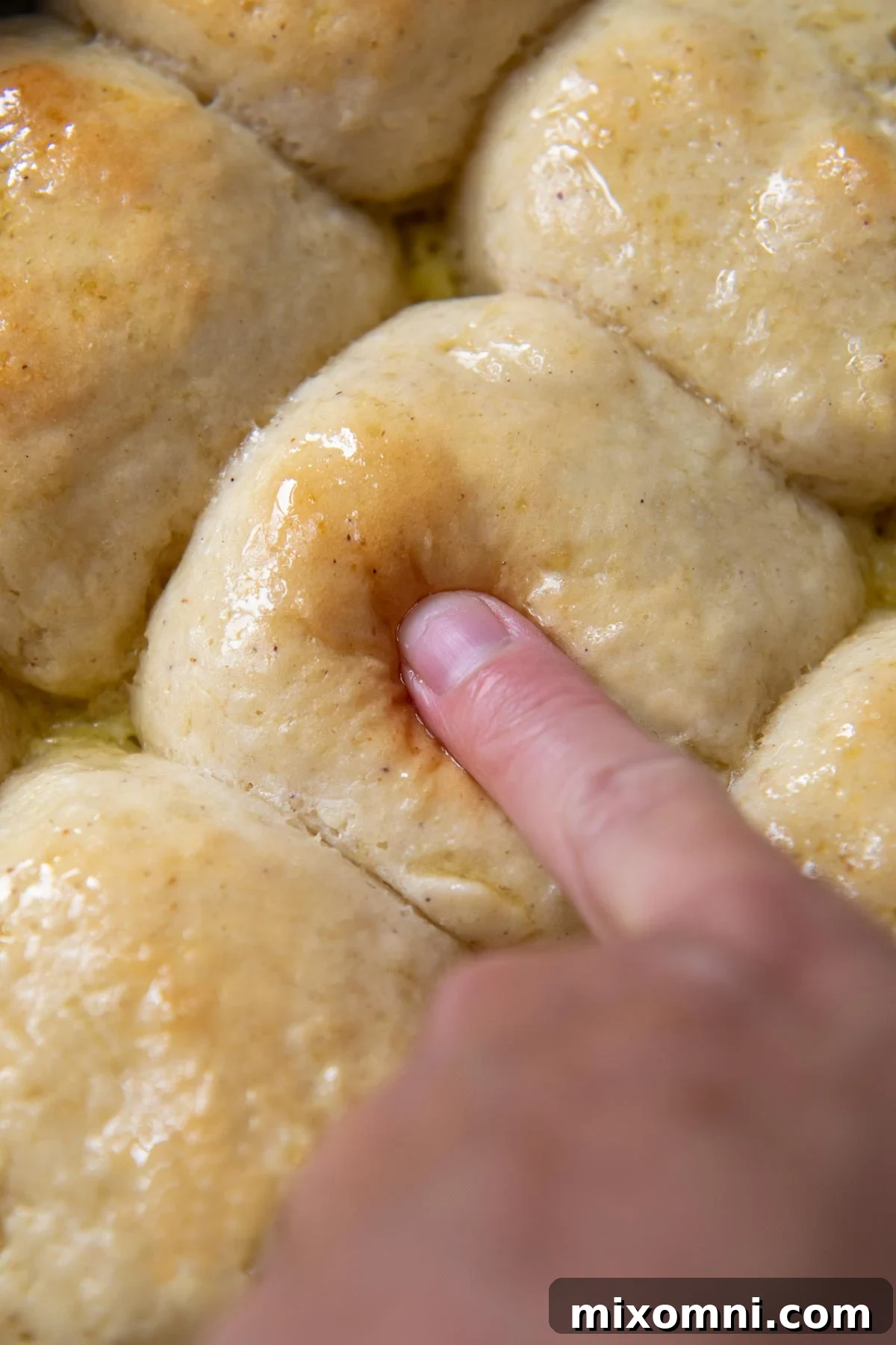 A finger gently pressing into the top of a freshly baked, soft gluten-free roll.