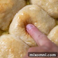 A finger pressing into the top of a roll, highlighting its squishy softness.