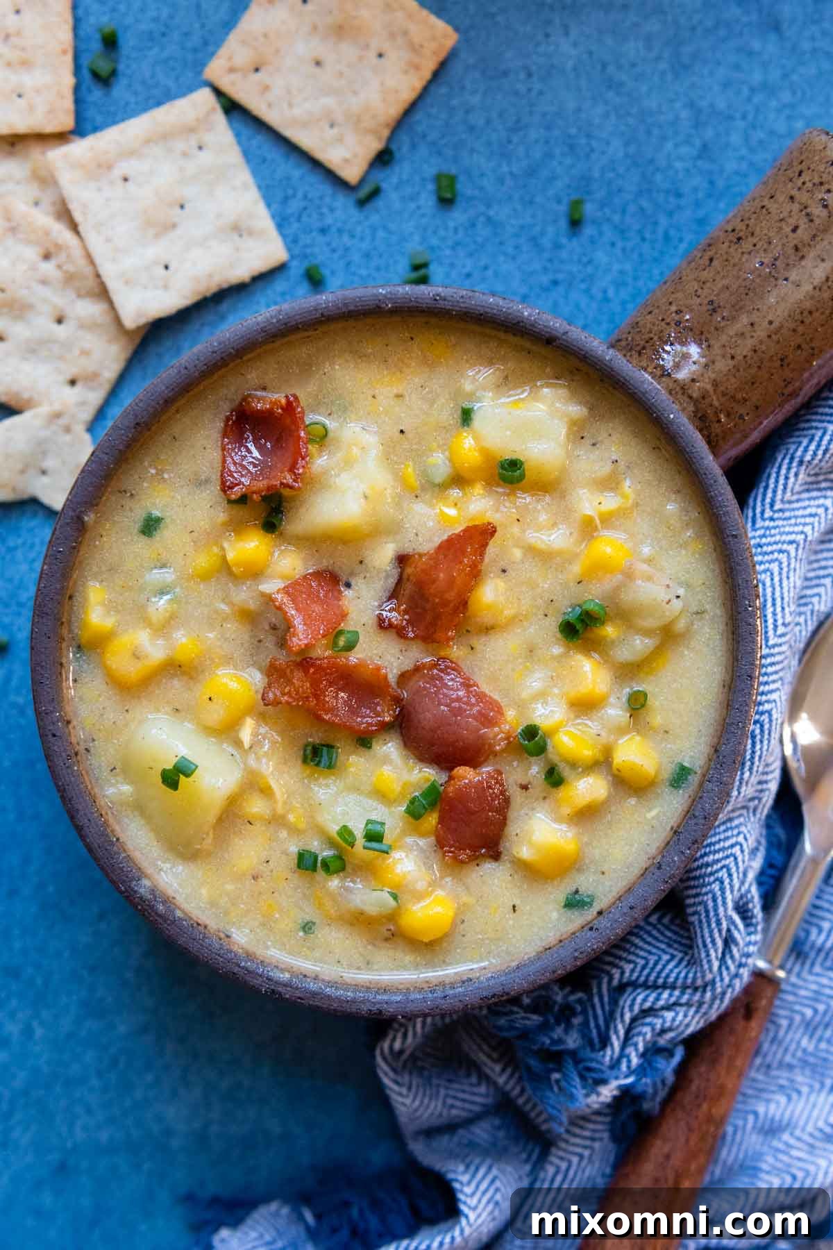 A beautifully presented overhead shot of thick and creamy gluten-free corn chowder, garnished with fresh chives and served with crackers scattered around. The perfect hearty meal for any season.
