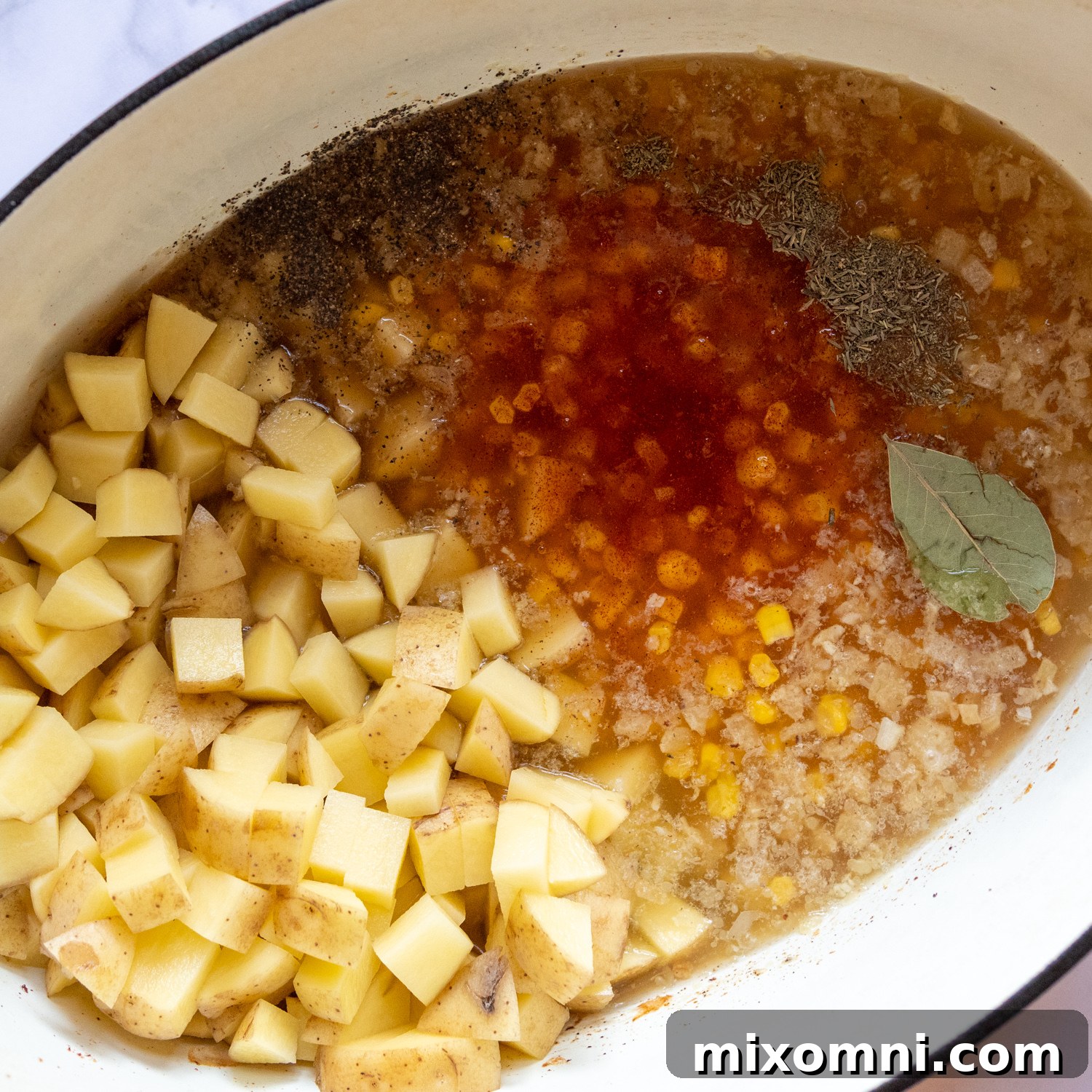 Potatoes, broth, and various spices being added to the pot with sautéed onions and garlic, preparing for the simmering phase of the corn chowder.