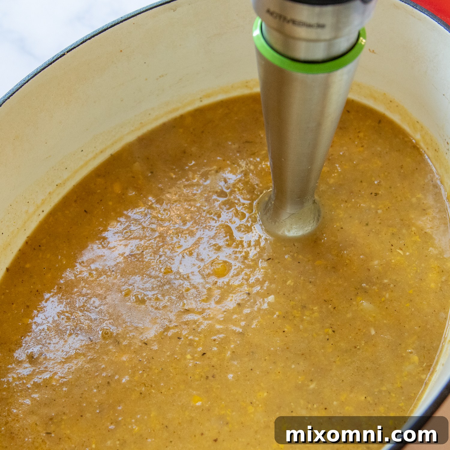 An immersion blender actively blending half of the corn chowder directly in the pot, creating a smooth and thick consistency for the soup.